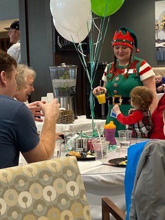 An elf holds up a balloon next to a family