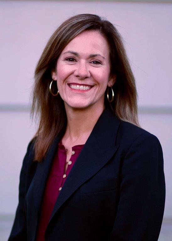 a headshot of a smiling woman with shoulder-length hair wearing a navy blazer and a burgundy blouse