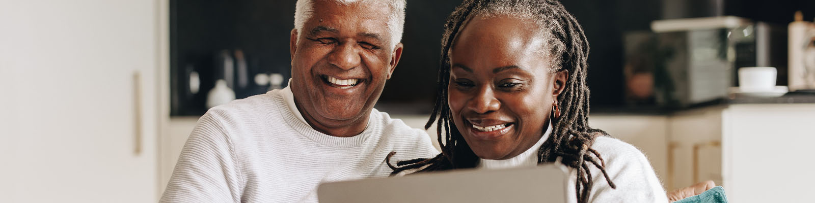 Senior couple sitting on a couch while smiling and looking down at a laptop