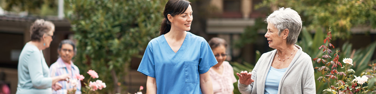 A female senior living resident talking with a female employee outside as other residents walk in the background