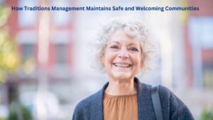 Senior woman with white hair wearing a mustard yellow shirt and a blue cardigan standing in front of a senior living apartment building smiling with text on the top of the image that reads "How Traditions Management Maintains Safe and Welcoming Communities"