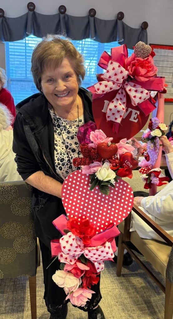 Smiling resident displaying a handmade Valentine’s Day floral craft at Traditions of Deerfield